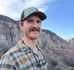 A man with a hat and a mountain range behind him