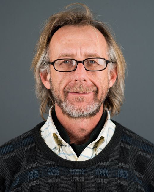 A man with glasses and a half smile, long hair