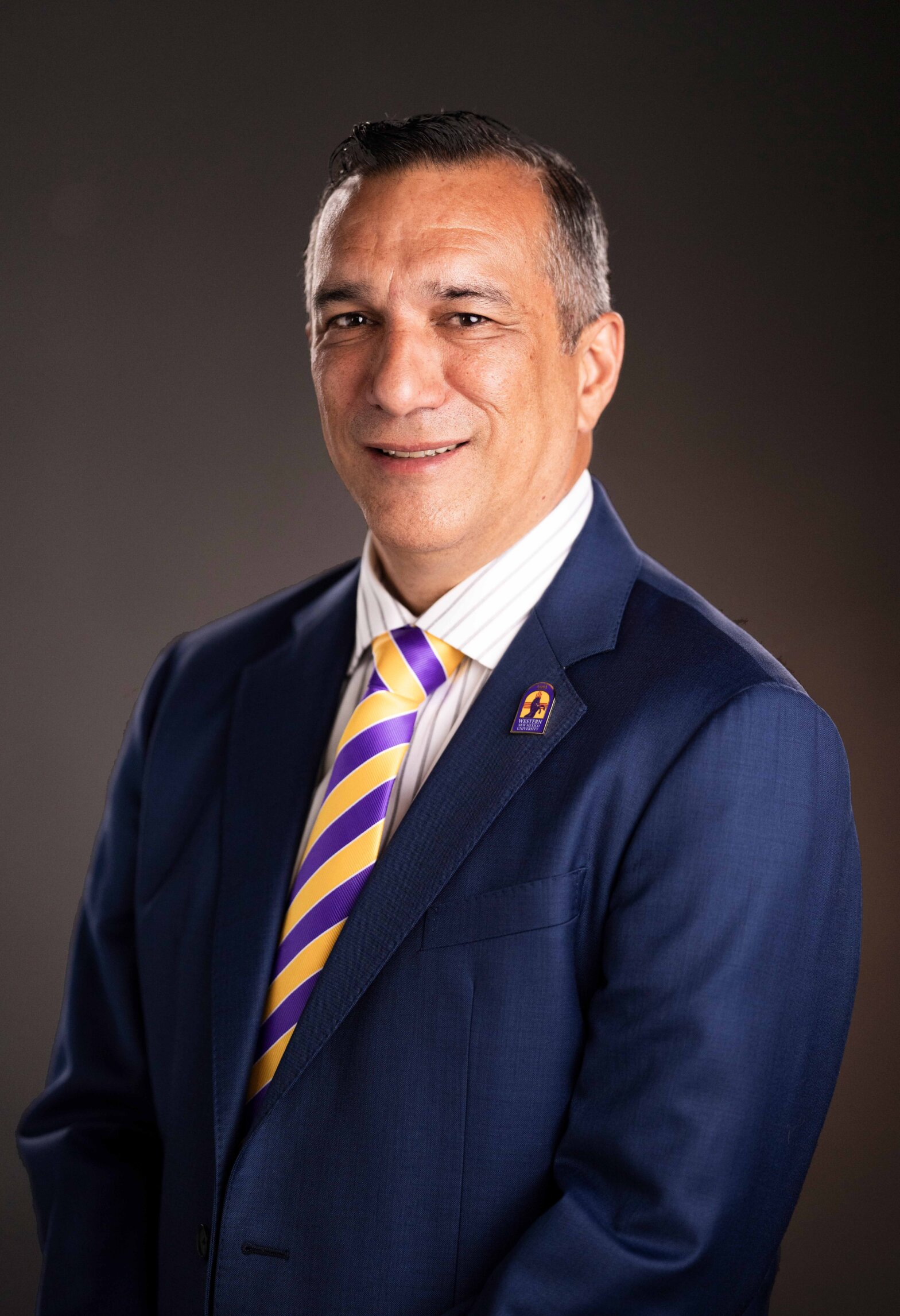 A man in a blue suit, and a striped tie, smiling at the camera.
