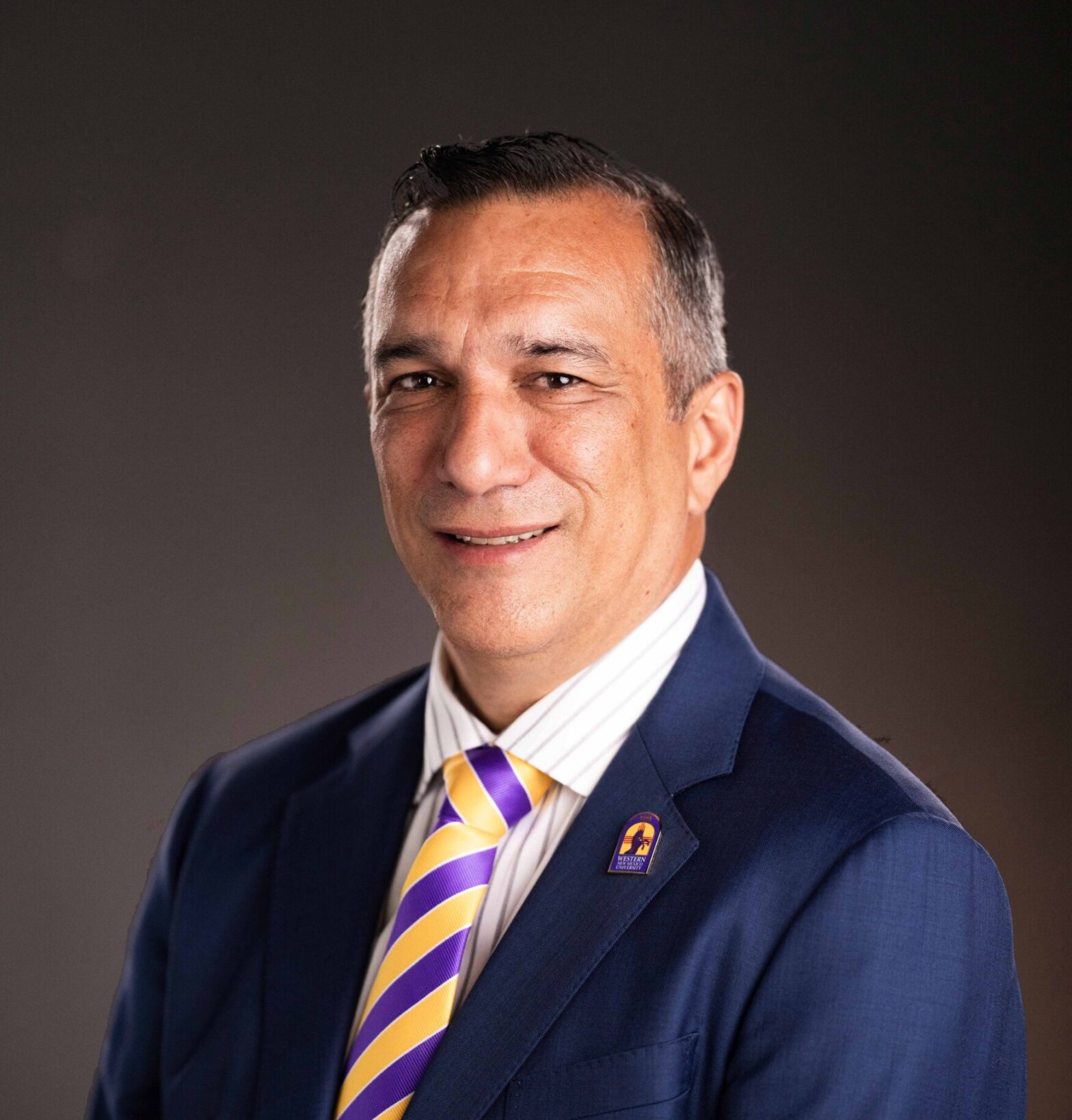 A man in a blue suit, and a striped tie, smiling at the camera.