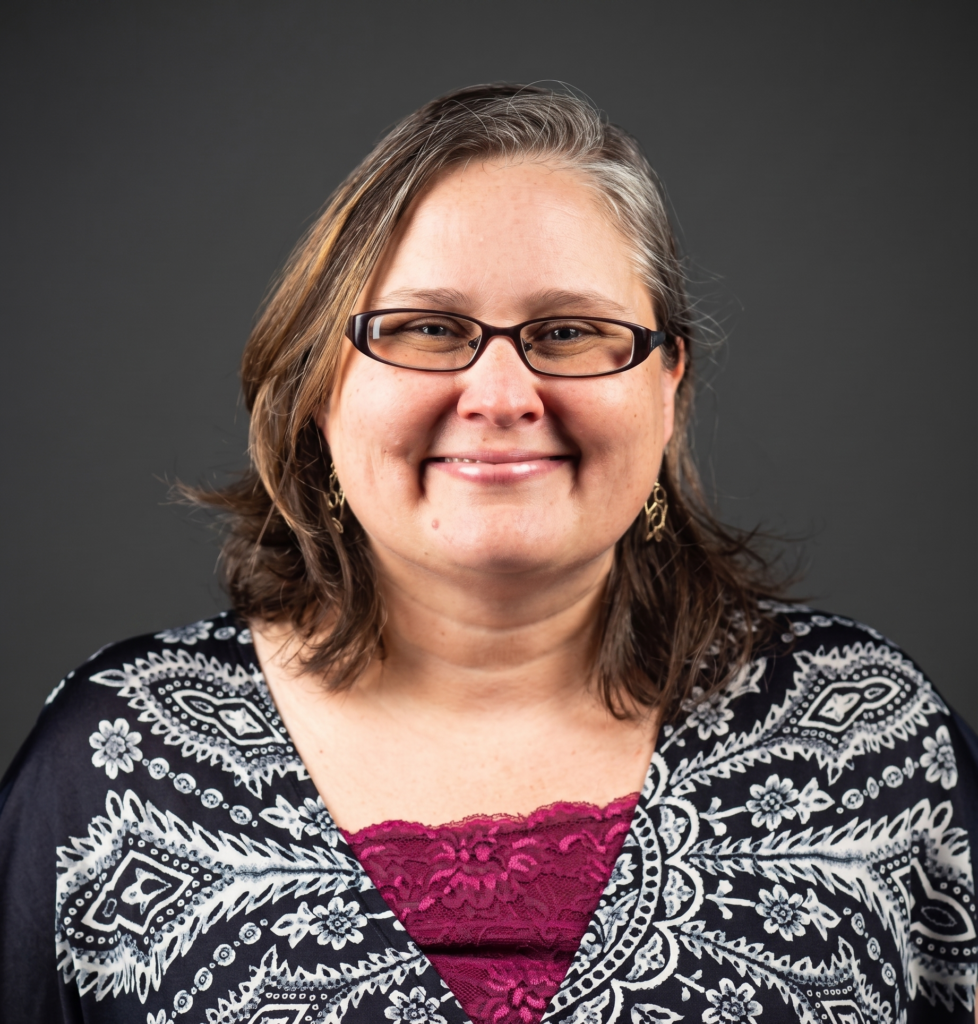 Woman with glasses and brown and grey hair, in a black and white jacket.