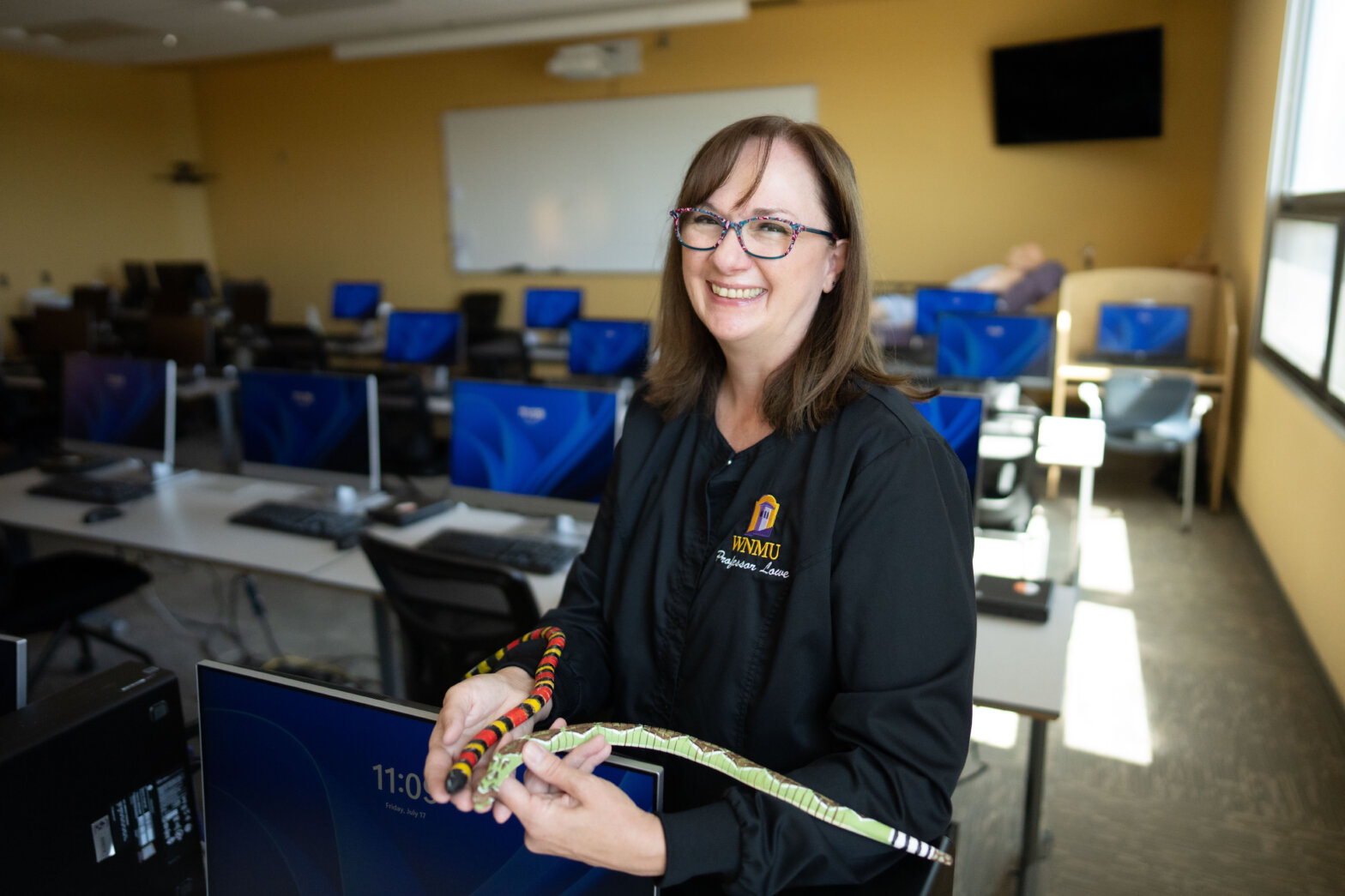 A female nurse with dark hair and glasses holds two separate types of snake models - one with red and black stripes, one with white and black stripes.
