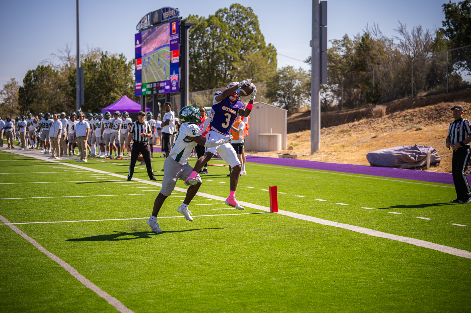 Two football players, one grabbing a thrown football, the other trying to stop him.