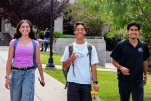 Three young people, a woman and two men, smiling and walking.