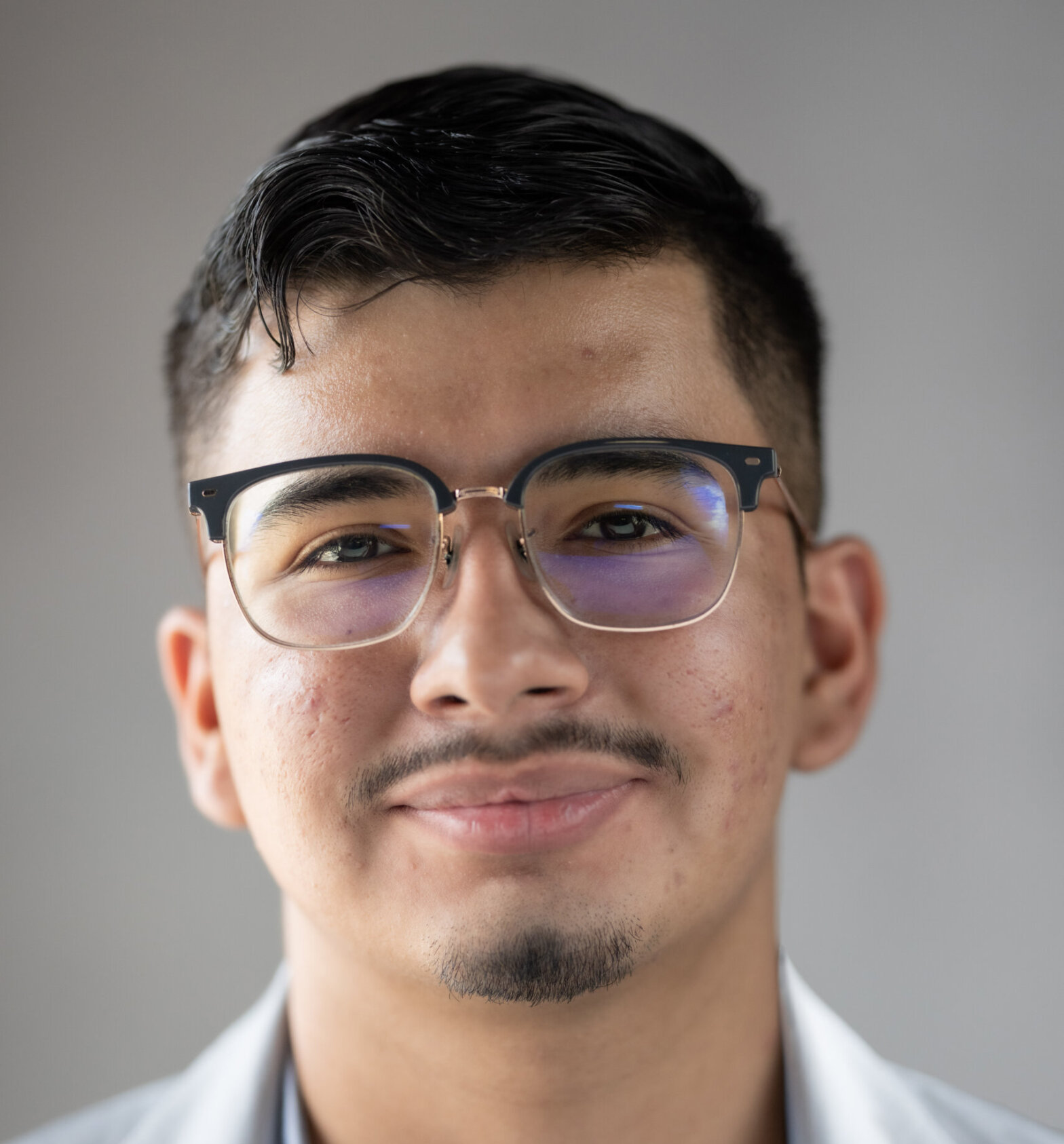 A young man with glasses and dark short hair smiles at the csmera