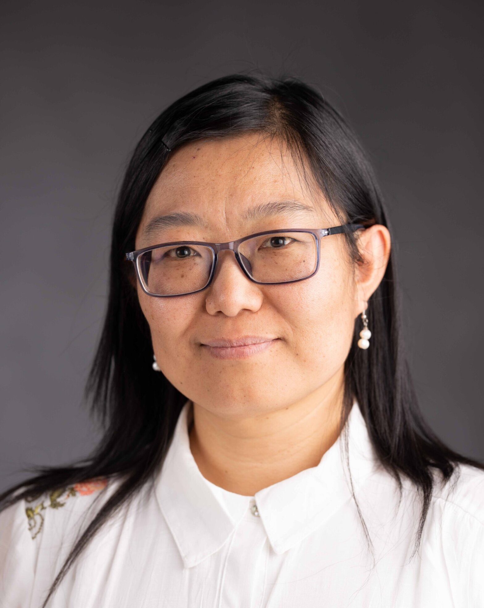A woman with long black hair and glasses, in a white shirt.