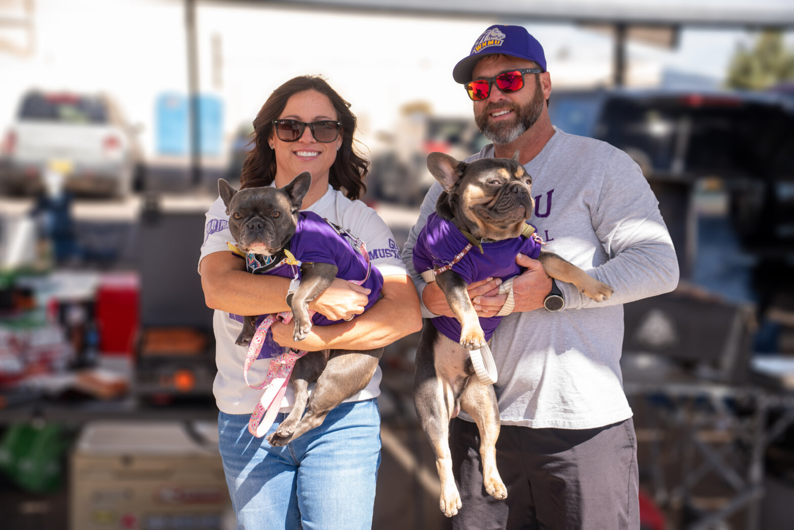 A woman and man holding two French bulldogs in their arms and smiling.